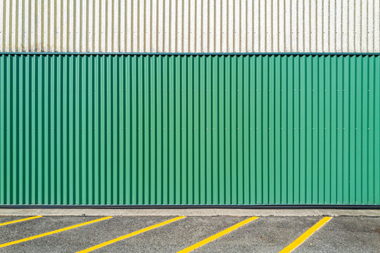 A green and white corrugated metal wall by a parking lot with painted stripes