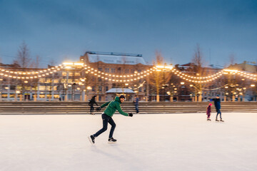 Obraz premium Horizontal shot of active man uses ice skates for going in for sport on ice ring, spends winter holidays actively, demonstrates professionalism and speed. Male ice skating outdoors