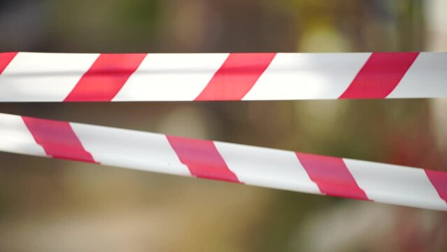 Red and white warning tape swinging in the wind. Protection sign. Don't cross the line. Red White caution tape pole fencing is protects for No entry. Backdrop without people, empty street. Close up