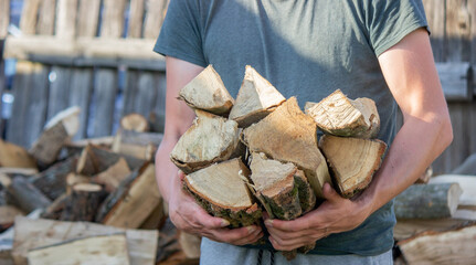 A man holds a lot of chopped firewood in his hands.