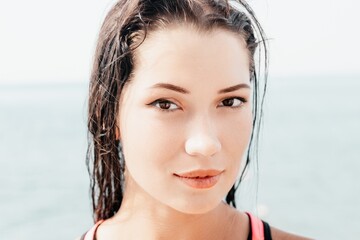 Woman sea sup. Close up portrait of beautiful young caucasian woman with black hair and freckles looking at camera and smiling. Cute woman portrait in a pink bikini posing on sup board in the sea