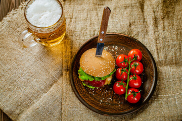 Top down view of homemade burger on rustic wooden serving table with glass of beer. Selective focus