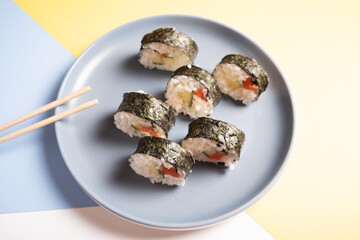 Sushi on a blue plate on a white, yellow and blue background.