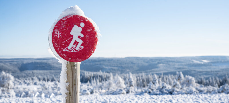 Red snowshoe hiking sign symbol with snovy trees and blue sky in winter snowscape landscape