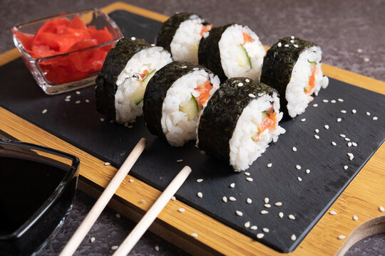 Sushi on a serving board with ginger, soy sauce and sprinkled with sesame.