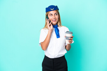 Airplane stewardess Uruguayan woman isolated on blue background holding coffee to take away and a mobile