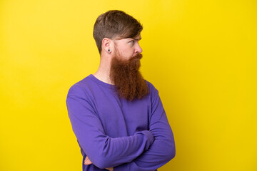 Redhead man with beard isolated on yellow background keeping the arms crossed