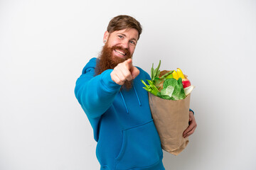 Redhead man with beard holding a grocery shopping bag isolated on white background pointing front with happy expression