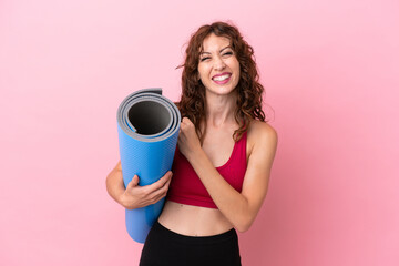 Young sport woman going to yoga classes while holding a mat isolated on pink background celebrating...