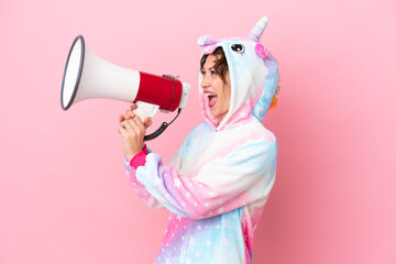 Young caucasian woman with unicorn pajamas isolated on pink background shouting through a megaphone