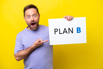 Middle age caucasian man isolated on yellow background holding a placard with the message PLAN B with surprised expression