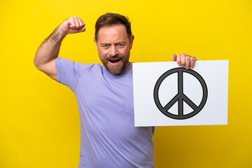 Middle age caucasian man isolated on yellow background holding a placard with peace symbol and...