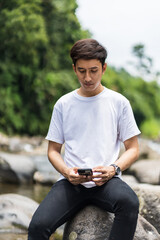 Fototapeta premium An Asian Man With White Shirt Browsing on His Smartphone in the Nature