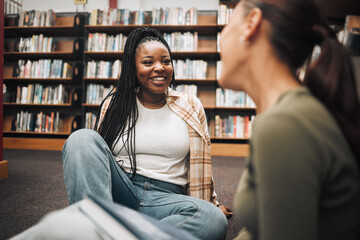 University, students and friends on library floor for studying, education and learning together. Happy black girl, gen z youth and college student at academy, campus and school in room with bookshelf - obrazy, fototapety, plakaty