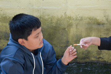 Boy learning to smoke with the same age friends in the area behind the school fence which teachers...