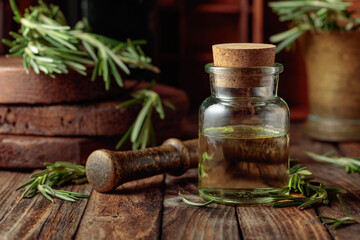 Rosemary essential oil or infusion on an old wooden table. - obrazy, fototapety, plakaty