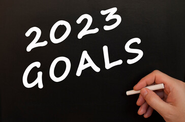 Male hand writes in chalk the words 2023 GOALS on a black board.