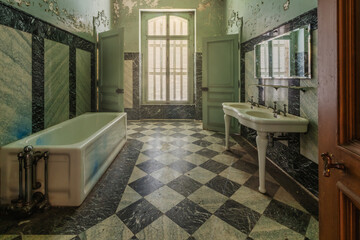 An old historic bathroom with checkerboard pattern on the floor and a large window.