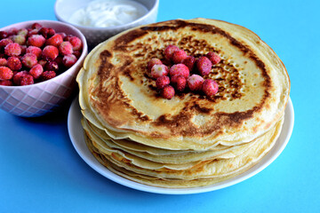 fried blini isolated on plate with frozen wild strawberries and sour cream