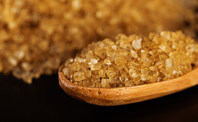 Yellow sea salt in a wooden spoon, highlighted on a black background. Close-up. Macro photography. Blurred background