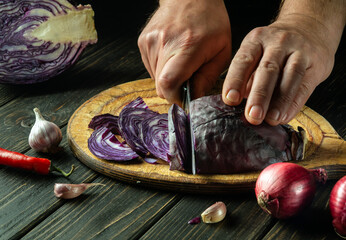 The cook cuts red cabbage on a cutting board with a knife. Cooking vegetable salad in the...
