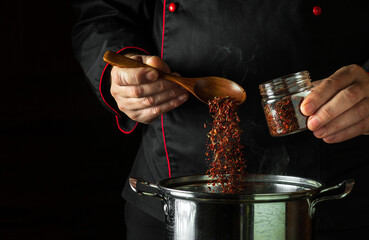 A professional chef adds dry red seasonings to a pot of boiling food. Retsoran kitchen cooking...