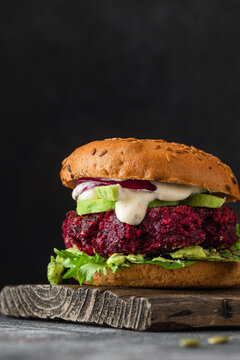 Veggie burger. Beet burger with vegan mayonnaise, avocado and onion on black background. Vegan diet food