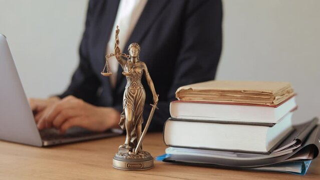 lawyer works on laptop in office, makes contract or agreement. attorney services online. statuette of themis on table in court. group consultations online on Internet.