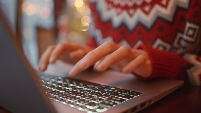 female hands types fingers by laptop keyboard, Businesswoman using laptop closeup. overworked woman in festive knitted sweater using laptop at coffee shop before christmas holidays