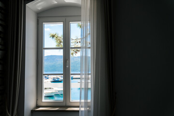 Window with view of sea and yachts. Cozy home interior in apartment. Ancient authentic house on coastline. Copy space on wall. Concept of calming summer vacation, travel