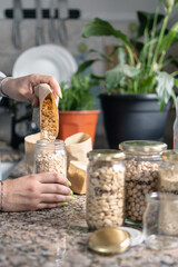 Close up of woman hand taking bulk food from paper bags and filling recycled jars. Sustainability and eco friendly lifestyle concept.