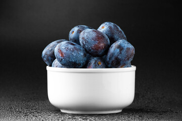 A handful of blue plums in a white plate on a dark background.
