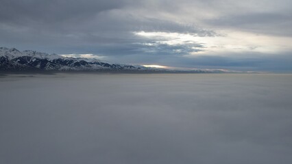 Flying a drone among the clouds with a view of the mountains. The light yellow rays of the sun at sunset are reflected on the surface of the clouds. Double layer of clouds. Mountains are visible
