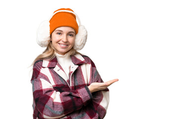 Young  English woman wearing winter muffs over isolated background presenting an idea while looking...