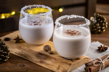 Christmas drink from raw eggs egg-nog on a wooden surface with a bokeh of rustic garlands