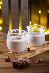 A traditional Christmas egg-nog drink made from raw eggs and milk on a light bokeh background from the lights of the garland. Two glasses of egg-nog close-up