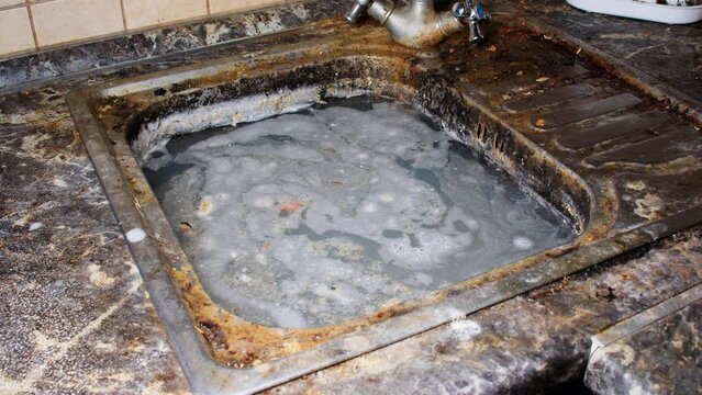 Very dirty sink. The kitchen sink is filled with soapy water, filled with food and grease. Old kitchen sink with dishwashing liquid. Washing dirty dishes. The unkempt kitchen needs cleaning. Close-up