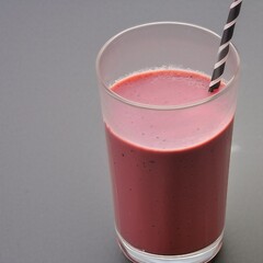 a drunk glass of pink smoothie on a table with a straw