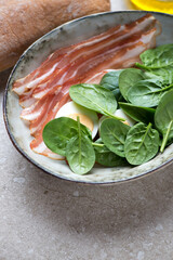 Bowl with fresh spinach leaves, bacon and boiled chicken eggs, vertical shot on a beige stone...