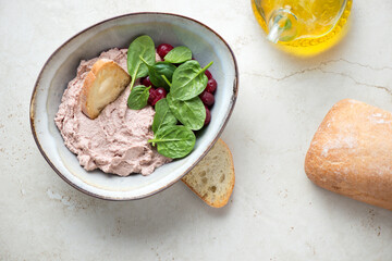 Bowl of liver pate with cranberry sauce, spinach leaves and ciabatta. Above view on a beige stone background, horizontal shot