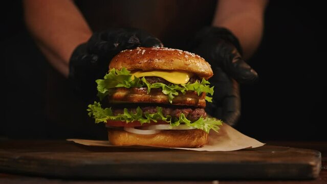 Beef burger serving. Hands of waiter serve chef burger on craft paper on table.