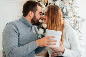 happy couple near gift boxes and christmas tree. couple embracing and looking at each other near christmas tree.