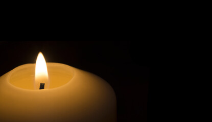 A candle lit in the dark.  Black background with a lit candle in the foreground