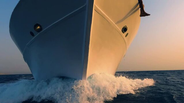 Sailboat prow breaking sea water front view, white foam and splashes close up. Yachting, ocean sailing, sunset sun light on vessel part, boat forepart closeup