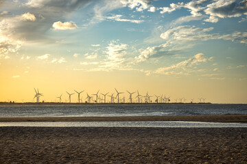 Fototapeta na wymiar Sunset on a tropical beach. In the distance a renewable energy farm