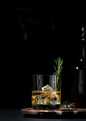Whiskey, scotch or bourbon glass with fresh rosemary, ice cubes on black background