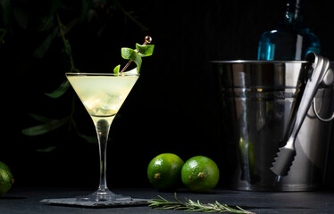 Gimlet alcoholic cocktail with dry gin, liqueur, lime juice and ice in glass garnished with lime zest. Black background