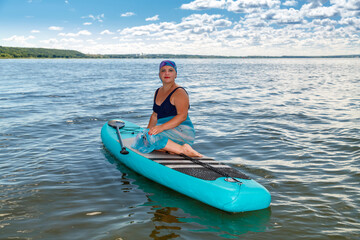 A woman with a Mohawk in a pareo on a SUP board in a lake against the background of white clouds on...