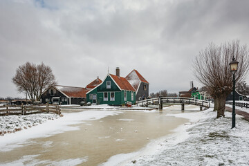 Winter landscape with frozen canal and traditional wooden house in Zaanse Schans, Netherlands - 554673032