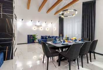 A modern living room with a blue sofa and a fixed table. Ceiling with wooden beams. Open space